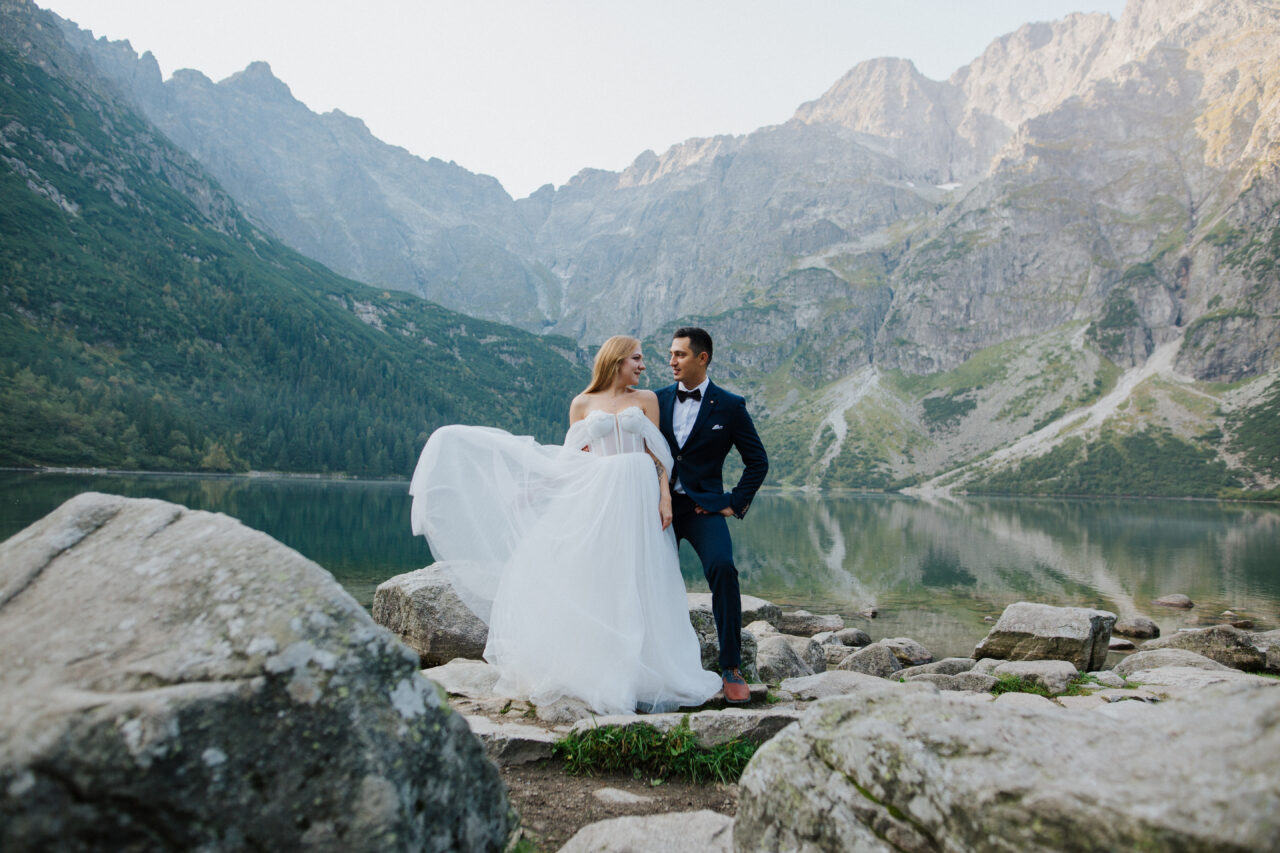 BODA EN LA MONTAÑA La novia mira a su novio, están parados en medio del marco, la hermosa naturaleza está detrás de ellos