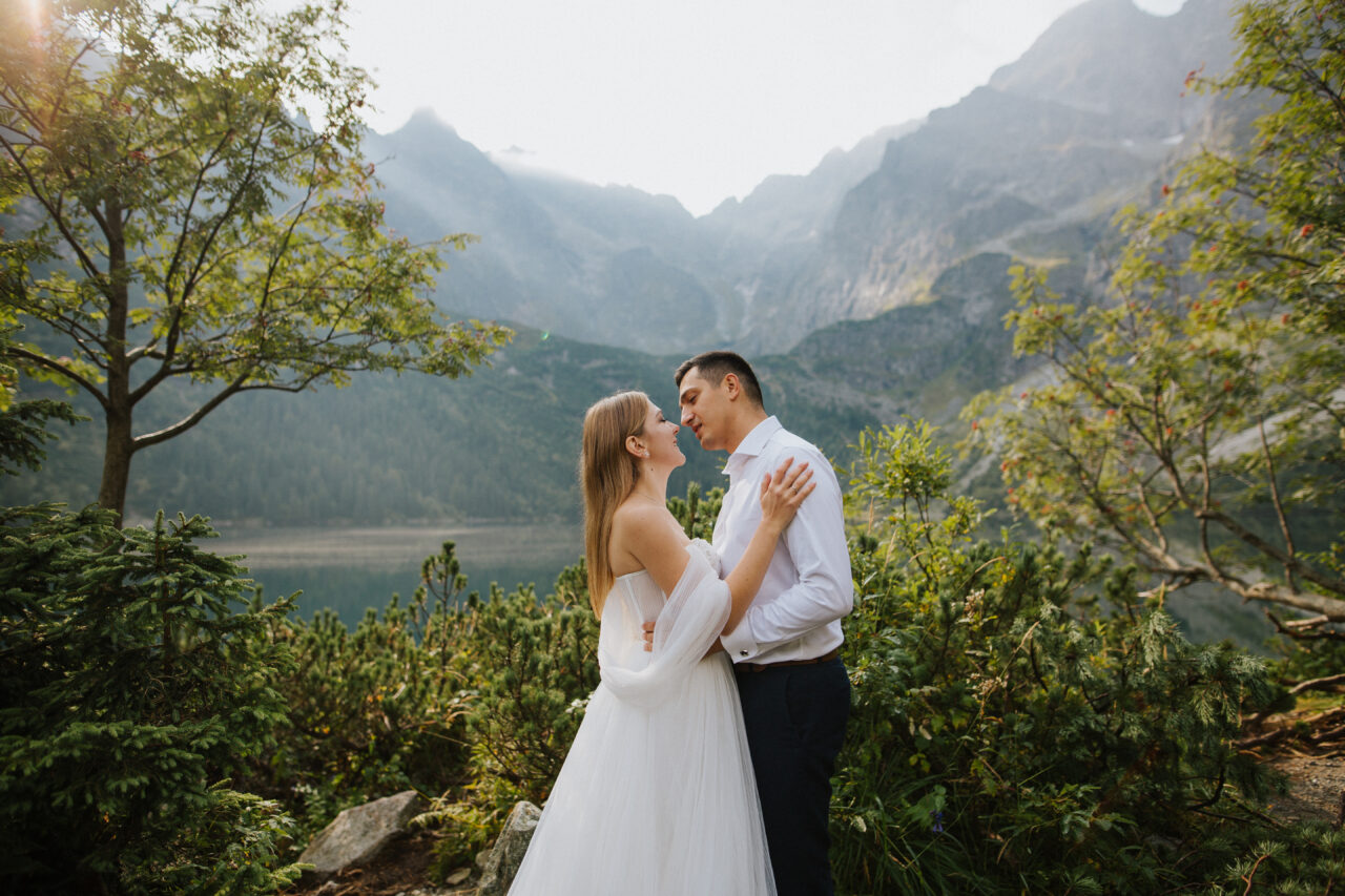 Foto de boda, la novia busca un beso con su novio. Se paran en el medio de la foto, que está en tonos cálidos y naturales.